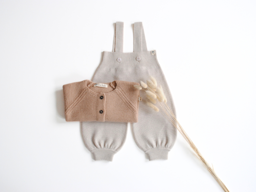 Latzhose für Babys in creme mit Cardigan in sand, beides aus Merinowolle